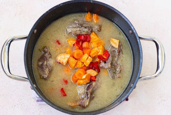 A pot of soup with tender beef ox tails, carrots, red peppers, and rich broth sits invitingly on a light background—a delightful hint for an easy oxtail recipe.