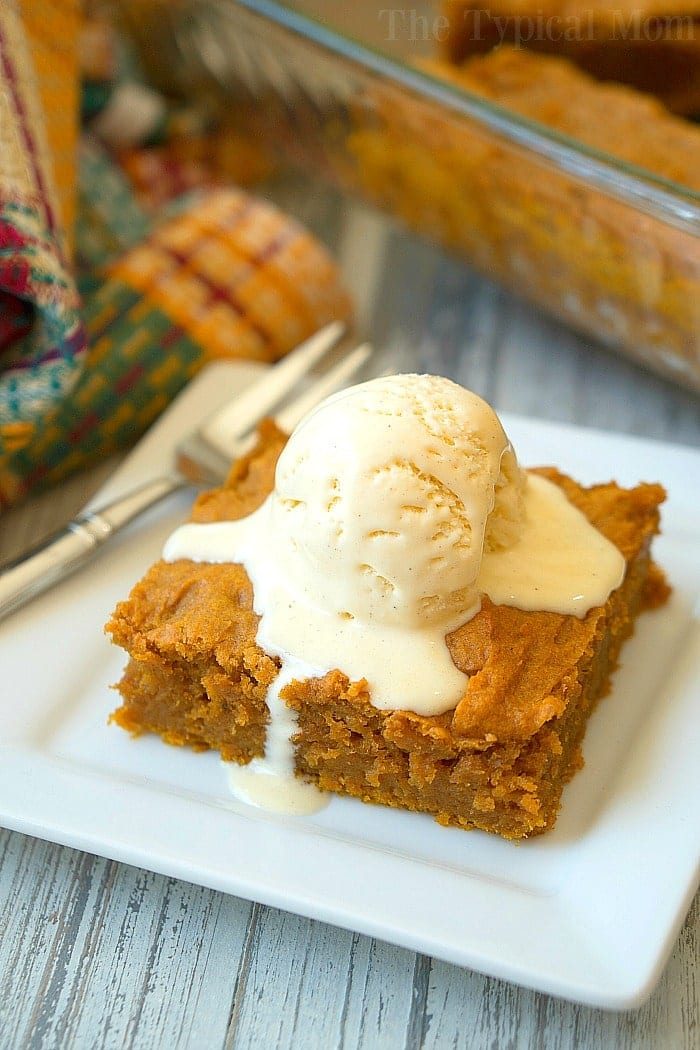 A delightful pumpkin pudding cake square topped with a scoop of vanilla ice cream sits on a white plate, with a fork beside it, reminiscent of an easy pumpkin pudding cake recipe.