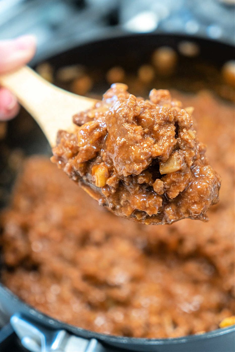 A wooden spoon holds a scoop of thick, chunky beef stew above a pot of the same stew—comfort food that's almost as simple as an easy sloppy joe recipe with 3 ingredients.