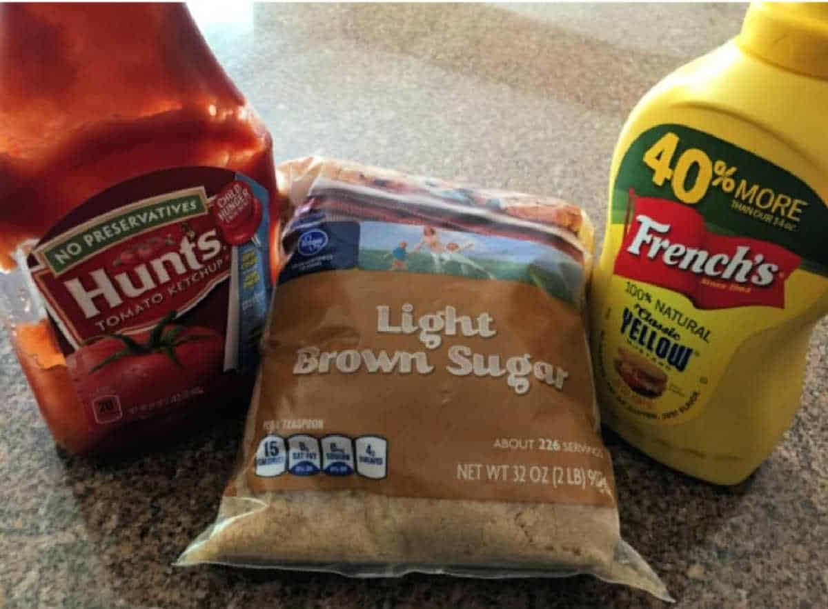A bottle of Hunt's ketchup, a bag of light brown sugar, and a bottle of French's yellow mustard on a counter—solid for an easy sloppy joe recipe with 3 ingredients.