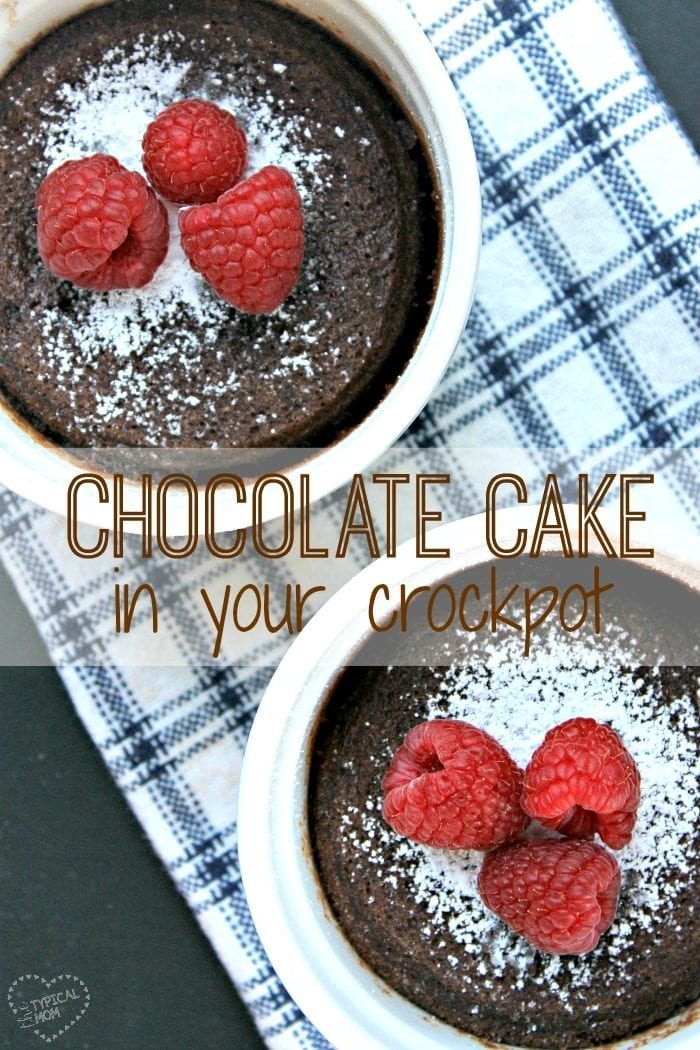 Two chocolate cakes in white ramekins, topped with powdered sugar and fresh raspberries, sit on a checkered blue and white cloth. The text reads Crockpot Cake – deliciously easy!