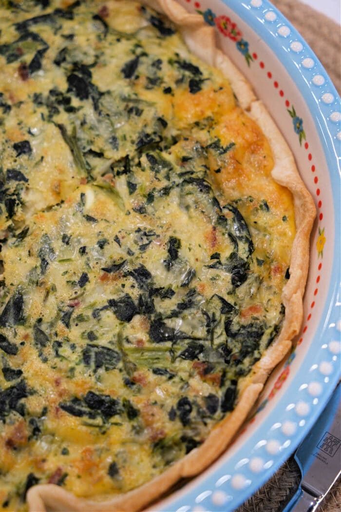 A close-up of a baked spinach quiche in a decorative pie dish with a golden, flaky crust—an easy spinach quiche recipe that's solid for any occasion.