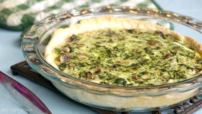 An easy spinach quiche recipe, this baked spinach and mushroom quiche sits perfectly in a glass pie dish on the table.