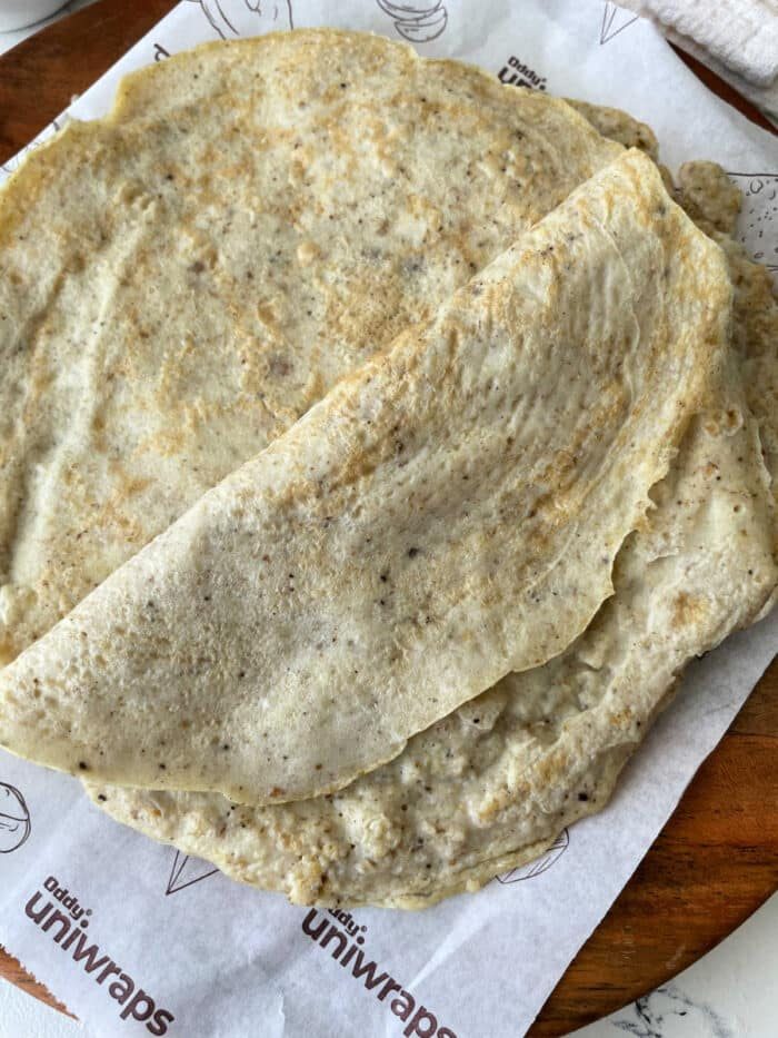 A stack of egg white tortillas sit elegantly on branded parchment paper atop a rustic wooden surface.