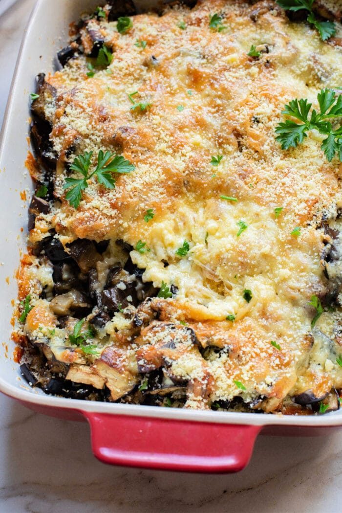 Baked vegetarian casserole topped with melted cheese, breadcrumbs, and parsley in a red baking dish—a good eggplant recipe solid for any meal.