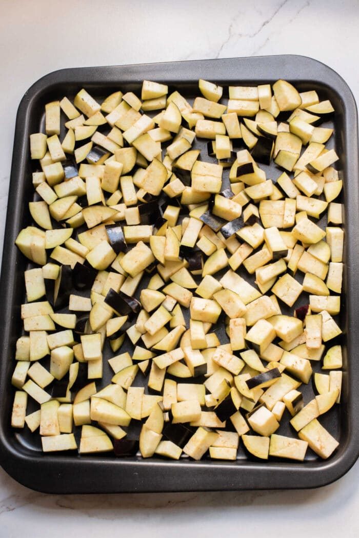 A baking tray filled with evenly spread, diced raw eggplant pieces on a light countertop—solid for starting your favorite eggplant casserole or trying a new eggplant recipe.