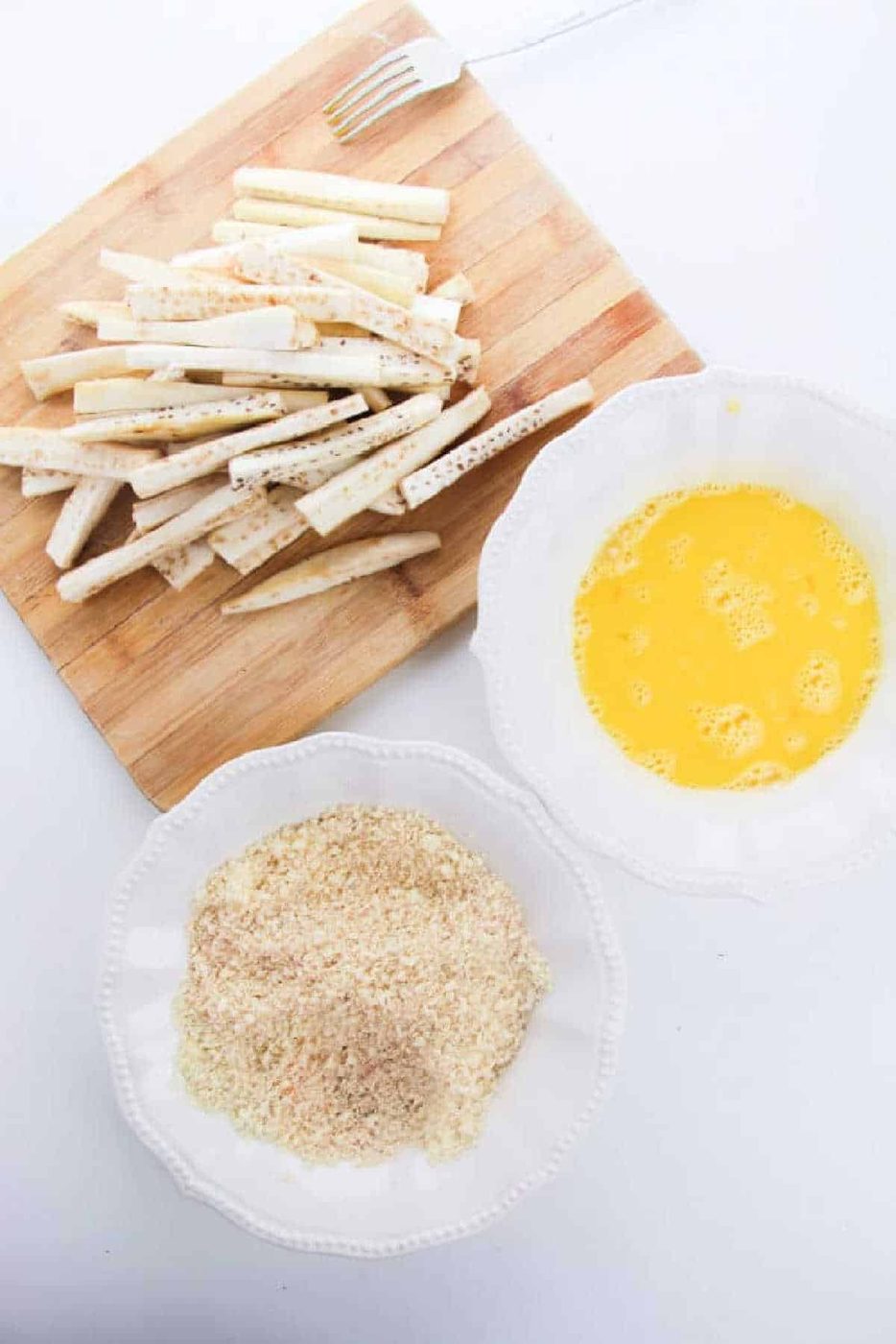 eggplant sticks on a cutting board, with bowls of beaten eggs and breadcrumbs next to them—solid for making unique alternatives to Eggplant Fries.