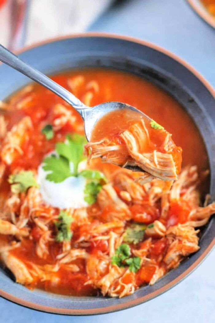 A bowl of chicken fajita soup with cilantro evokes the hearty flavors of fajita soup, as a spoon lifts a savory portion.