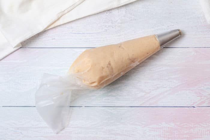 A piping bag filled with churro dough lies invitingly on a white wooden surface, ready to make air fryer chocolate-filled churros.
