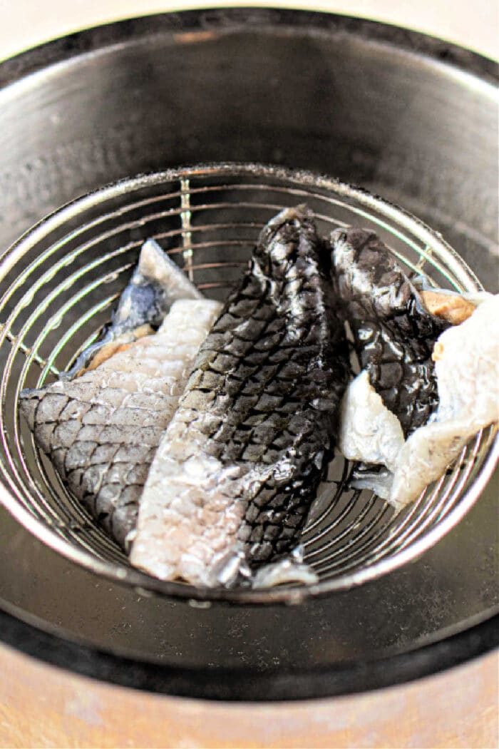 Gently place the crispy fish skins in a wire strainer over a metal pot.