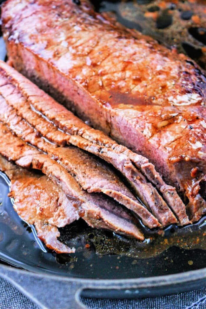 Sliced roasted flank steak nestled in a cast iron pan with flavorful juices.