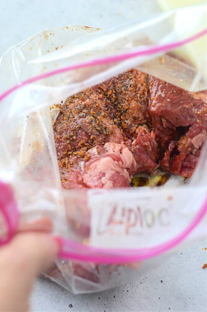 Flank steak with spices and marinade in a Ziploc bag, ready to be sealed before sizzling on a cast iron skillet.