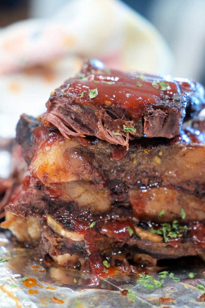Close-up of saucy, tender Flanken Short Ribs stacked on foil, garnished with chopped herbs—an irresistible Short Ribs Recipe.