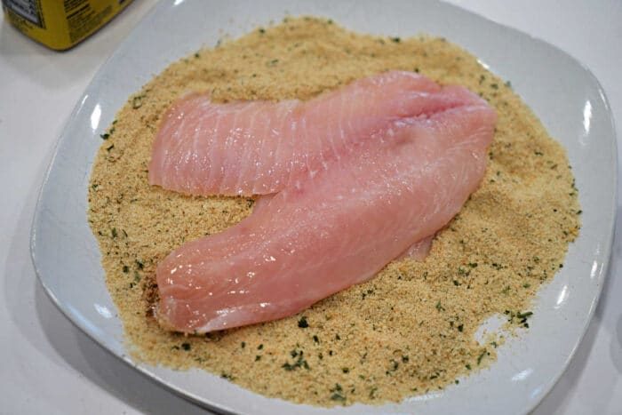 Raw fish fillets on a plate of seasoned bread crumbs, ready for coating and cooking—a classic start to any good Fried Tilapia recipe.