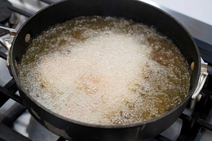 A black pan on a stove with fried tilapia deep frying in bubbling hot oil, solid for your next tilapia recipe.