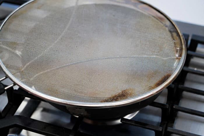 A frying pan on a stove, covered with a metal mesh splatter screen, is solid for preparing your favorite fried tilapia recipe.