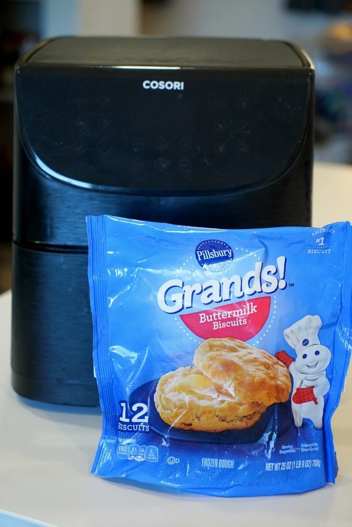 A Cosori air fryer sits behind a blue bag of Pillsbury Grands! Buttermilk Biscuits on the counter, ready to show how easy it is to make frozen biscuits in an air fryer.