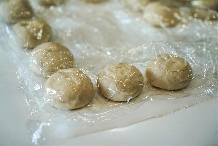 Small dough balls covered with plastic wrap, reminiscent of the shape of a delightful air fryer chicken cordon bleu, are neatly arranged in rows on a surface.