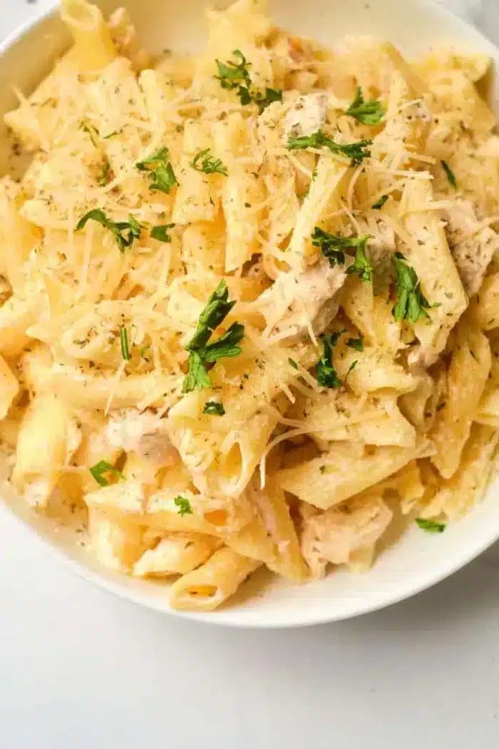 A bowl of creamy pasta topped with grated cheese and garnished with chopped herbs. The penne, mixed with a luxurious sauce, offers the comfort of homemade flavors, reminiscent of an Instant Pot creation.
