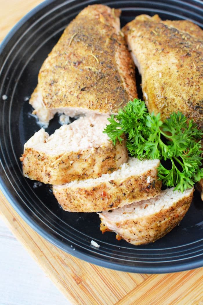 Sliced chicken breast with herbs, roasted to perfection like a frozen chicken breast in the oven, and elegantly garnished with parsley on a sleek black plate.
