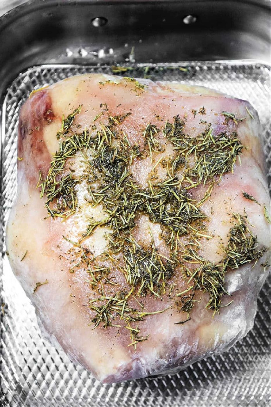 Raw lamb roast covered with herbs and seasonings in a metal roasting pan, ready to cook like if you were preparing frozen chicken in oven for a hearty meal.
