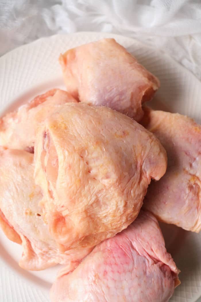 A pile of raw chicken thighs on a white plate, ready to be cooked as frozen chicken thighs in an air fryer.