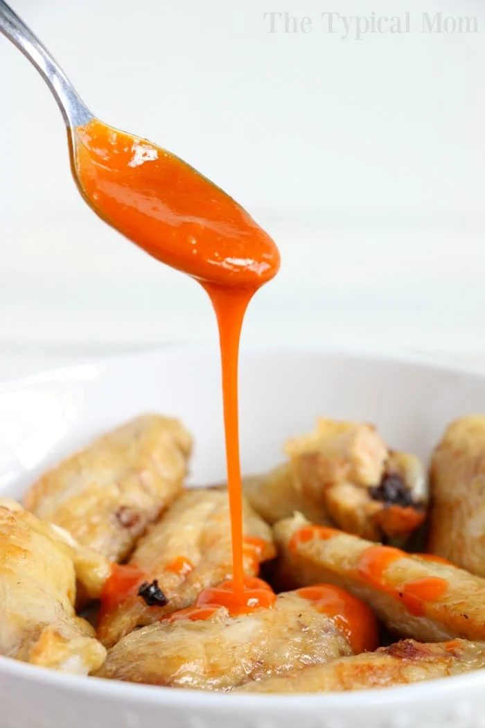 Spoon drizzling bright orange sauce over a bowl of crispy chicken wings straight from the air fryer.