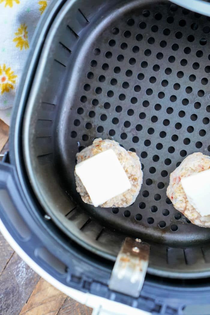 Two frozen crab cakes with butter on top in an air fryer basket, reminiscent of the ease of cooking frozen crab cakes in an air fryer.