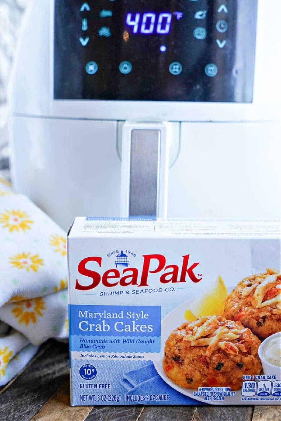 A box of SeaPak Maryland Style Frozen Crab Cakes sits in front of an air fryer displaying a 400°F temperature, ready for good results with the Frozen Crab Cakes in Air Fryer method.