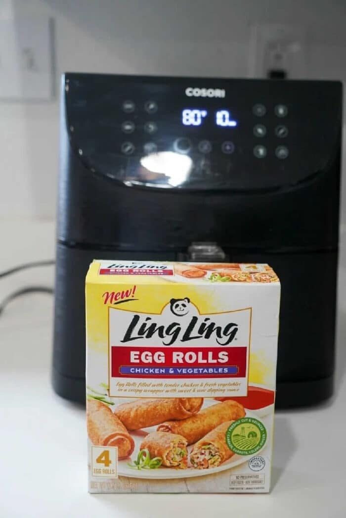 Box of Ling Ling chicken & vegetable egg rolls in front of a Cosori air fryer on a kitchen counter—solid for making good frozen egg rolls in air fryer with ease.