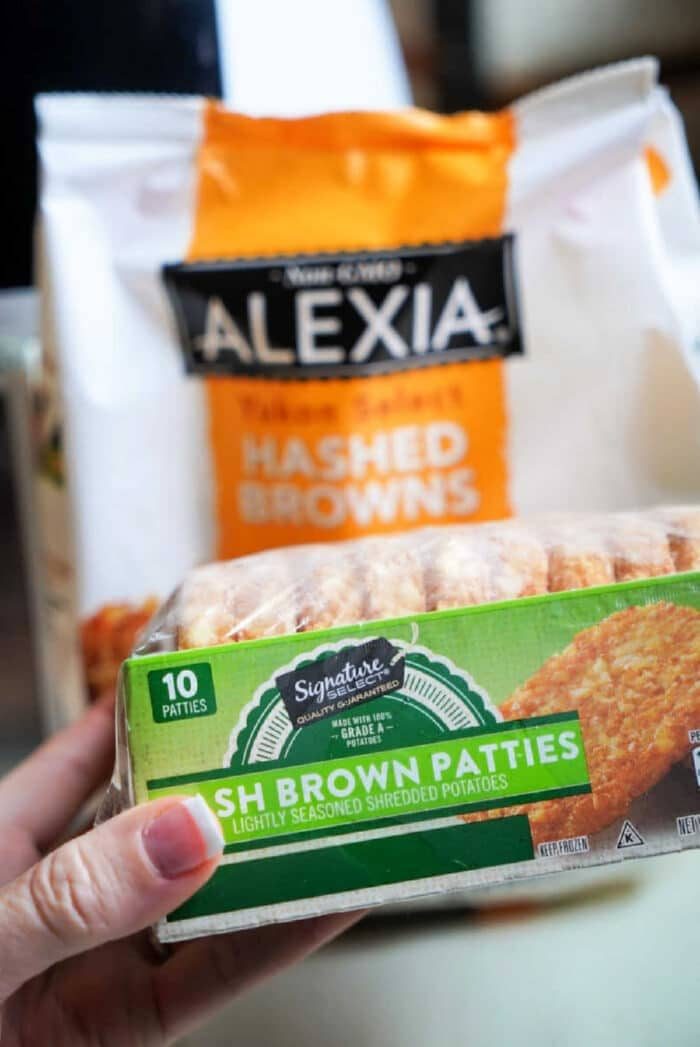 Close-up of a person holding a box of frozen hash brown patties in front of a bag of Alexia hashed browns, ready to be crisped to perfection in an air fryer.