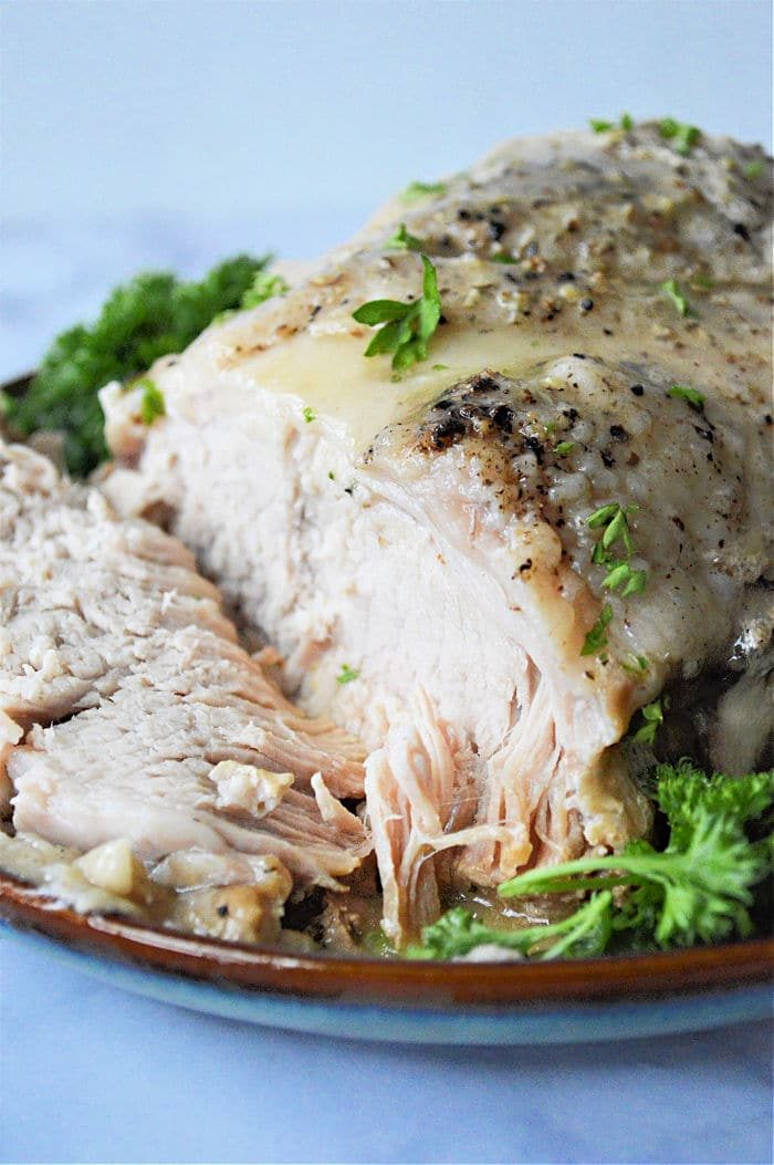 Sliced seasoned pork roast from frozen, prepared in an instant pot, is garnished with parsley on a plate.