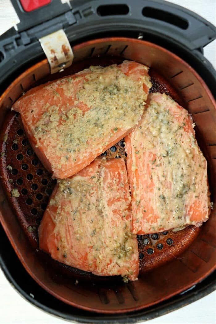 Three seasoned fillets of frozen salmon in air fryer basket, cooking to tender perfection.