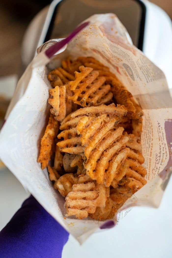 A person proudly holds a bag of frozen seasoned waffle fries, perfectly crispy from the air fryer.