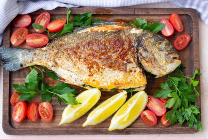 Enjoy a perfectly cooked whole fish served on a wooden board, garnished with lemon wedges, cherry tomatoes, and parsley—a delightful alternative to frying a whole fish.