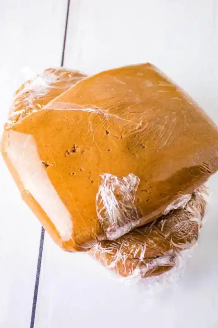 Three stacks of gingerbread dough wrapped in clear plastic wrap are placed on a white surface.