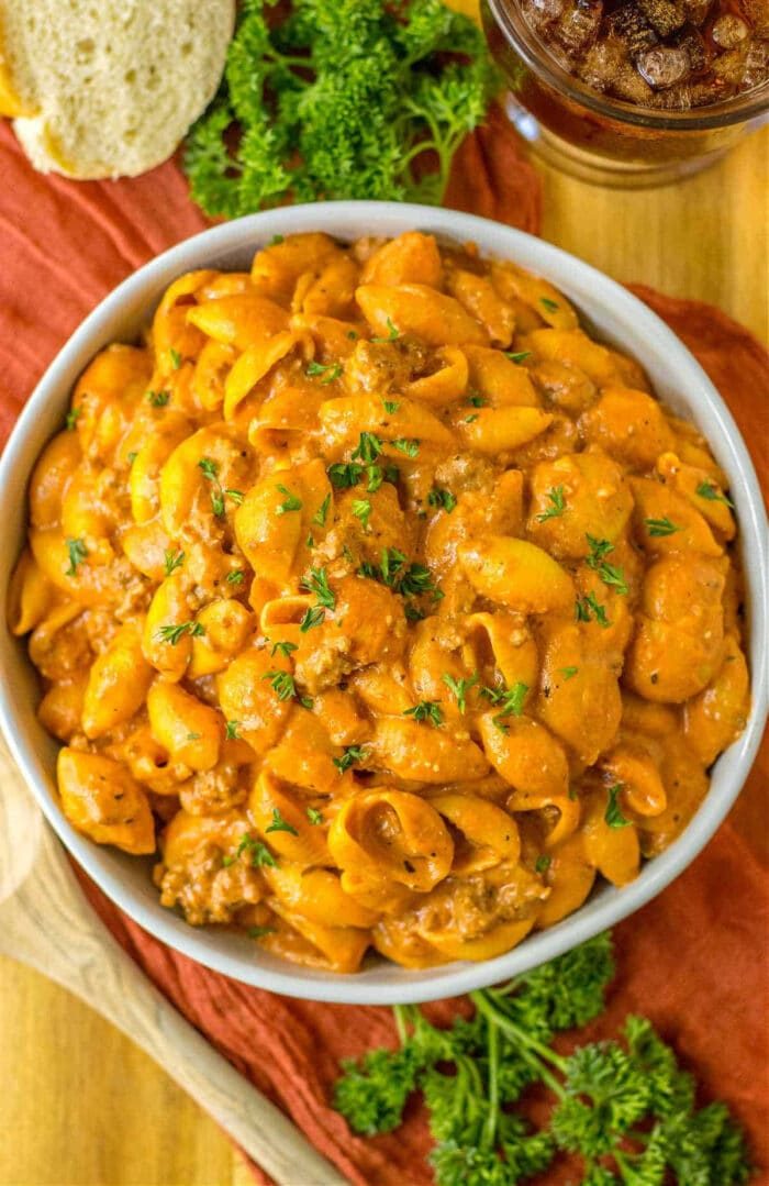 A bowl of creamy goulash in the Crock-pot with ground meat, garnished with chopped herbs, sits on a wooden table with fresh parsley nearby.