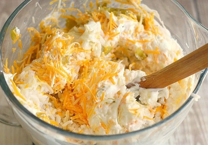 A clear bowl of cheesy green chile casserole mixture with a wooden spoon, infused with the vibrant zest of green chile rice.