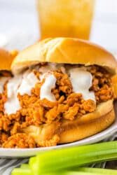 Close-up of slow cooker ground chicken sloppy joe sandwich with creamy sauce on a bun, next to a few celery sticks.