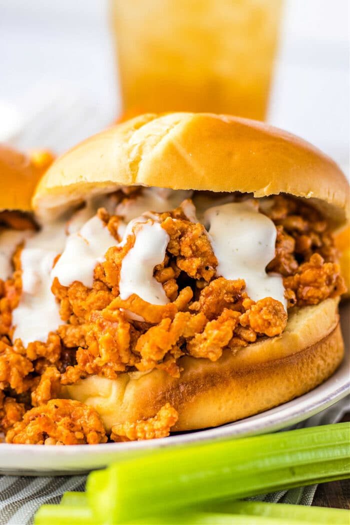 Close-up of ground chicken sloppy joe sandwich with creamy sauce on a bun, next to a few celery sticks.