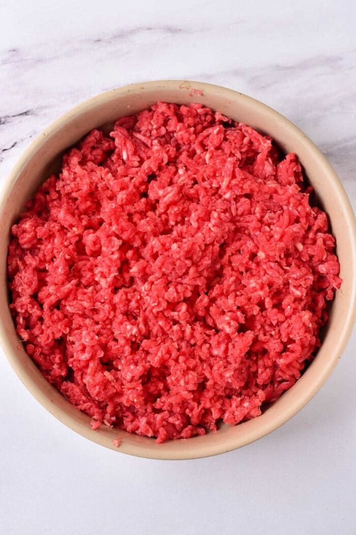 A bowl filled with raw ground deer meat sits on a marble countertop, ready to inspire your next culinary creation or ground venison recipes adventure.