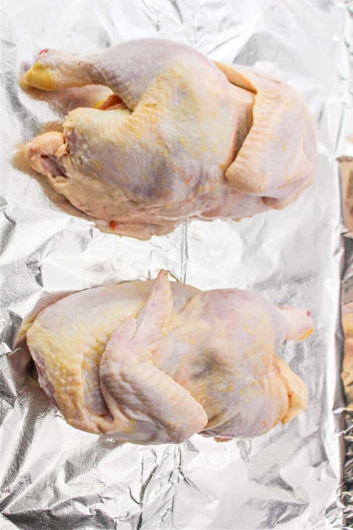 Two raw half chickens rest on aluminum foil, ready for preparation.