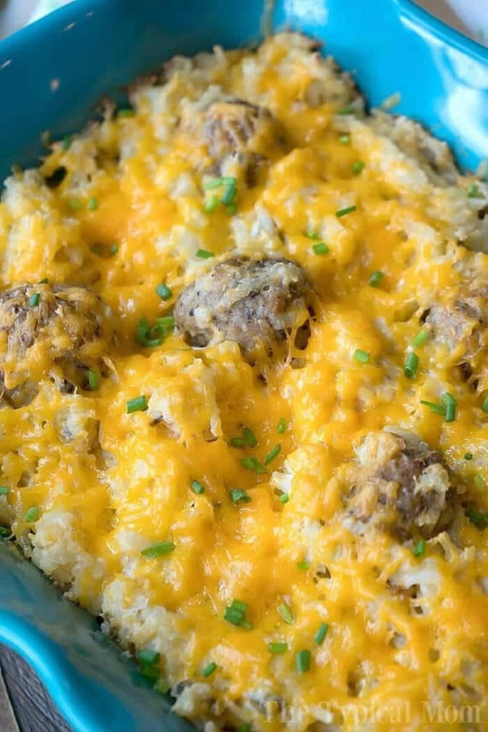 Baked hamburger hashbrown casserole with sour cream, melted cheese, savory meatballs, and chopped chives in a blue dish.