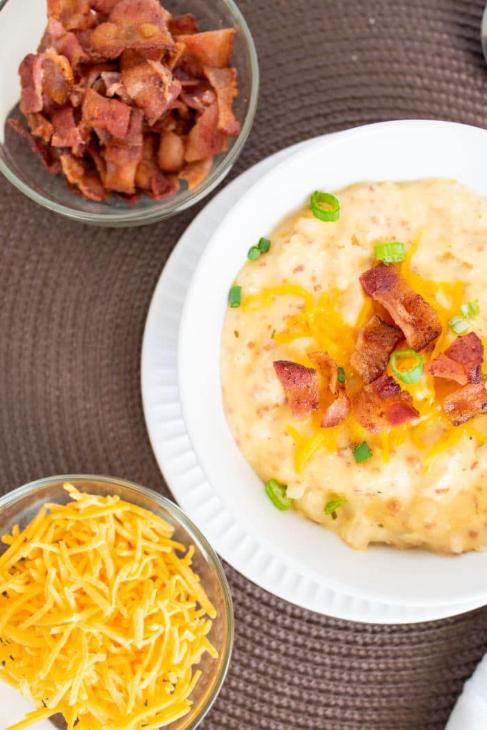 A bowl of loaded potato soup with bacon, cheese, and green onions pairs perfectly with the comforting flavors of hashbrown soup, surrounded by extra bowls of crispy bacon and shredded cheese for added indulgence.