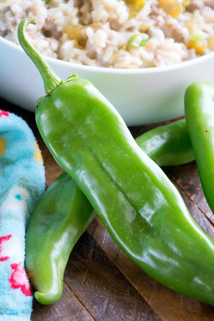 Fresh hatch green chili peppers rest on a wooden surface, hinting at the spicy twist in your instant pot sausage rice casserole, with a bowl of cooked rice in the background.