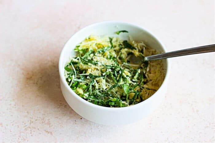 A bowl of vibrant greens, topped with slices of herbed crusted chicken, and a fork rests invitingly on the light surface.