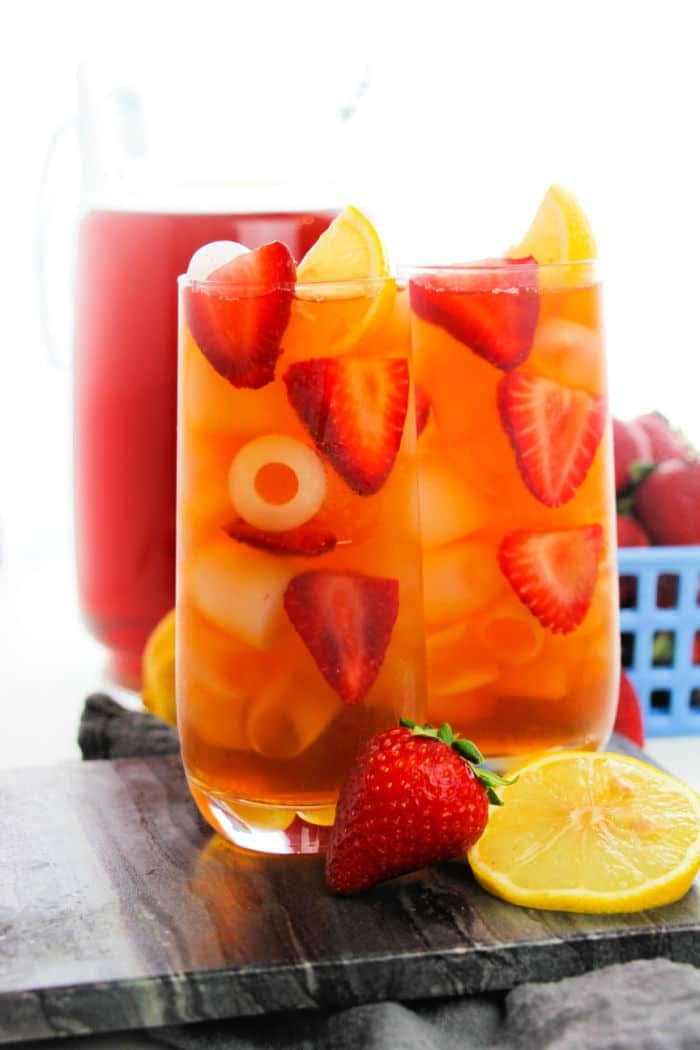 Two glasses of iced strawberry tea with lemon slices, infused with a hint of hibiscus sweet tea, rest on a wooden board.