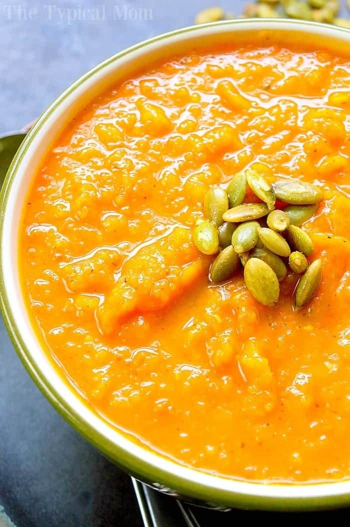 Close-up of creamy butternut squash carrot soup topped with pumpkin seeds in a bowl.