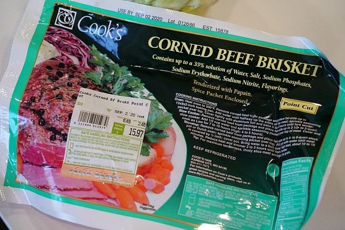 A package of Cooks Corned Beef Brisket is displayed. The label indicates it contains a 35% solution of water, salt, and other ingredients. An image of the cooked product with vegetables graces the packaging.