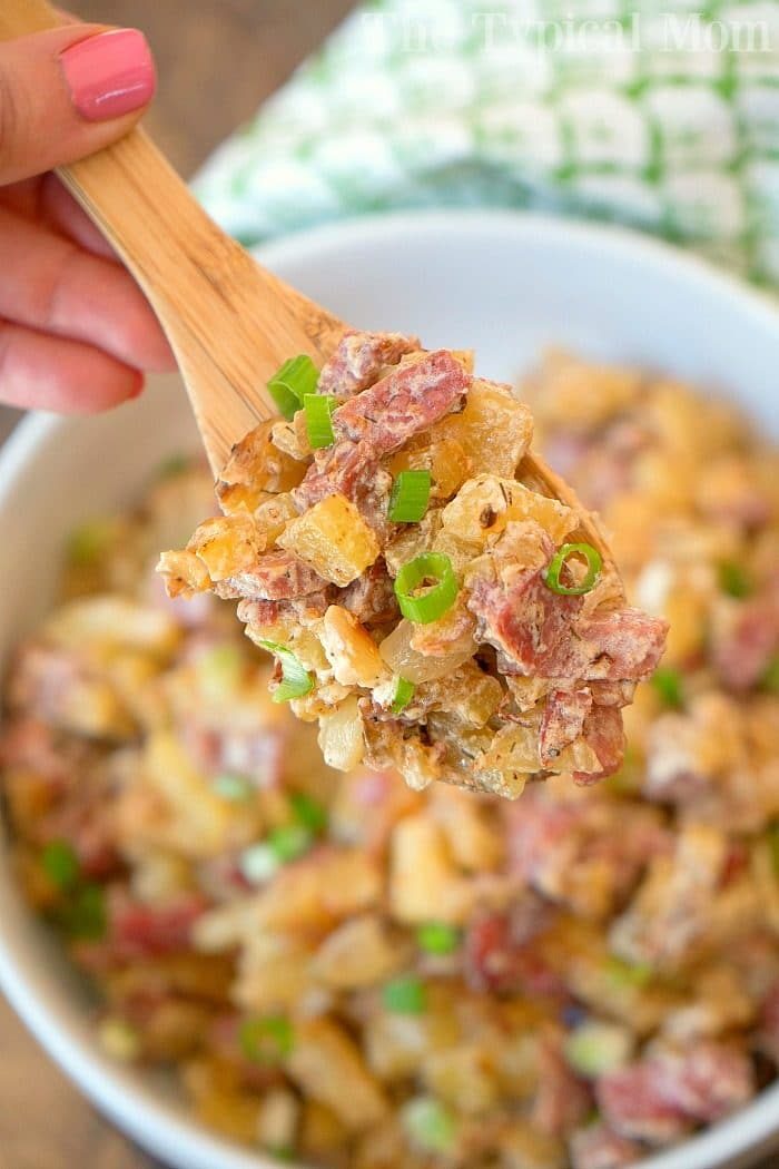 Close-up of a wooden spoon with creamy corned beef hash garnished with green onions, solid alongside your favorite homemade corned beef hash recipe.